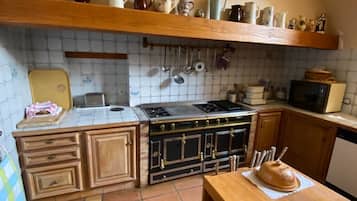 A kitchen with a stove, oven, and microwave. There are cabinets and a table with a loaf of bread.