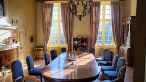A formal dining room with a large oval table, blue upholstered chairs, and a chandelier. - Château de Lauresse (Lombron)