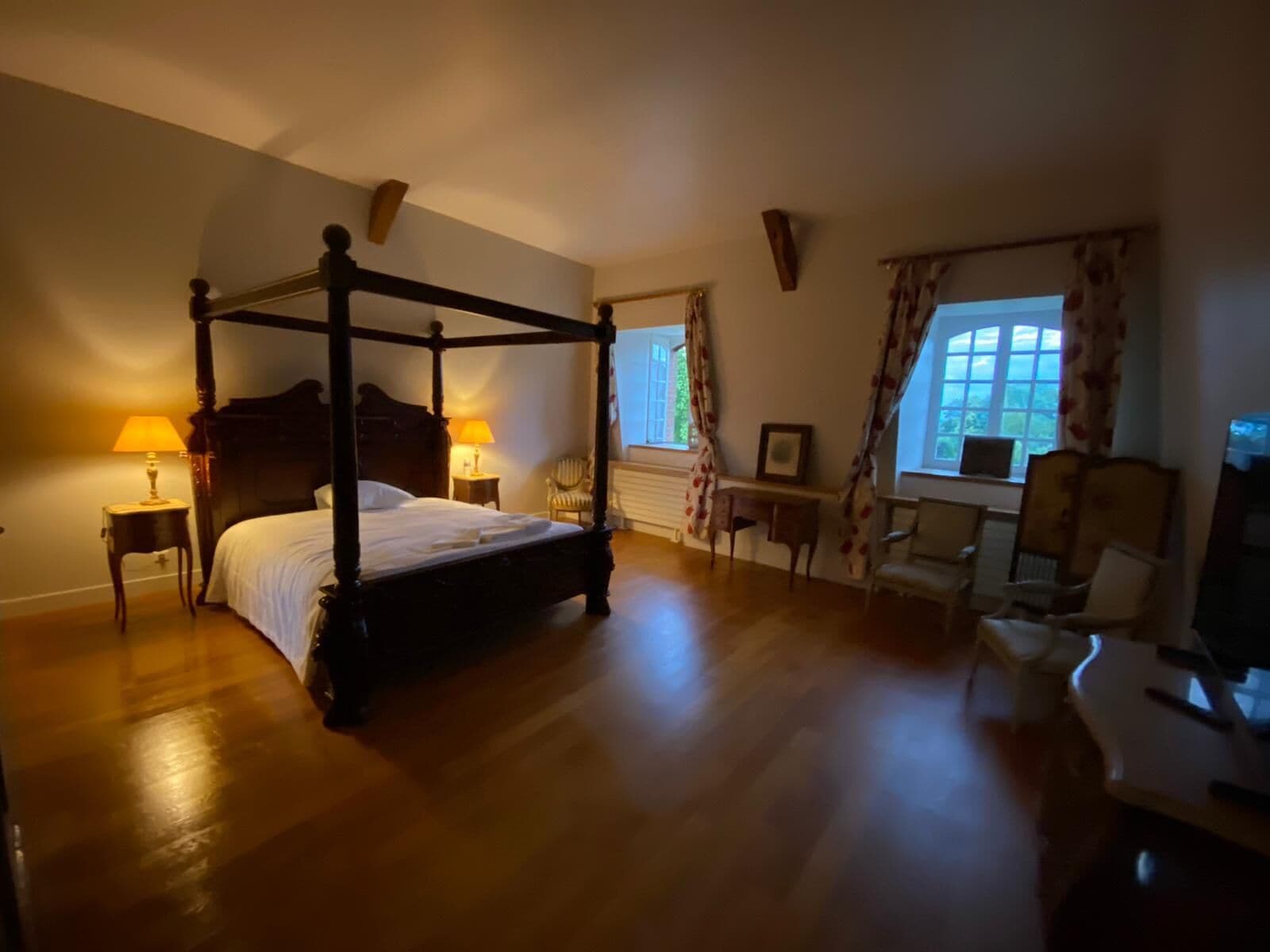 A four-poster bed with two bedside tables, a chair, and a desk with a chair.