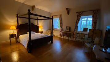 A four-poster bed with two bedside tables, a chair, and a desk with a chair.