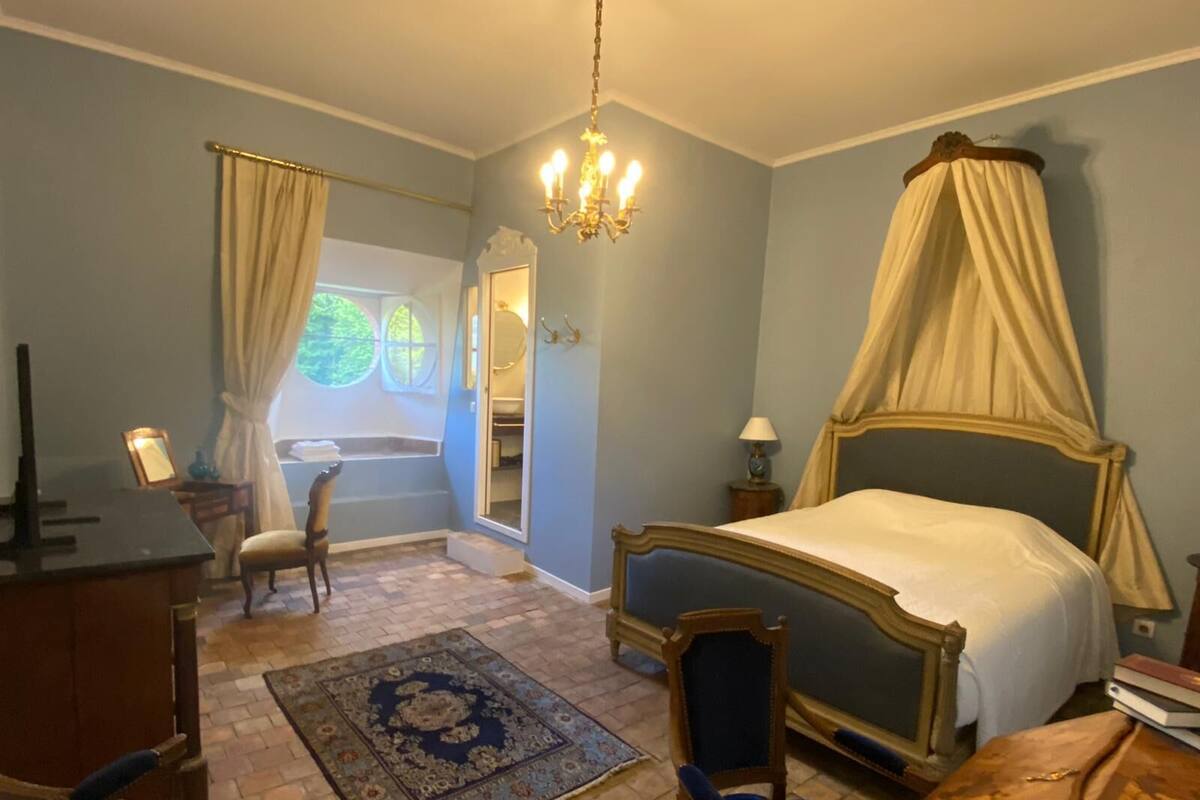 A bedroom with a four-poster bed, a desk, a chair, a rug, and a large mirror.