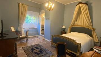 A bedroom with a four-poster bed, a desk, a chair, a rug, and a large mirror.