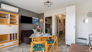 Un espacio habitable compacto con comedor, sofá, televisión y cocina al fondo.