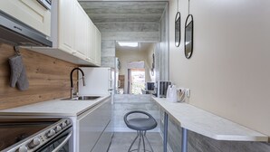Una cocina moderna con armarios blancos, una estufa y un lavamanos. Hay un taburete y una tetera sobre la encimera.