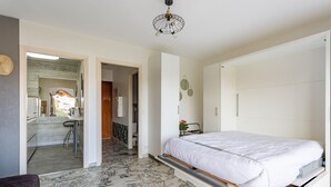 Un dormitorio con cama, armario y baño a la vista, visible a través de una puerta abierta.