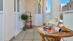 A balcony with a wooden table, a potted plant, a pair of sunglasses, a wine glass, and a croissant on a plate. - Hedera Estate, Hedera A38 (Dubrovnik)