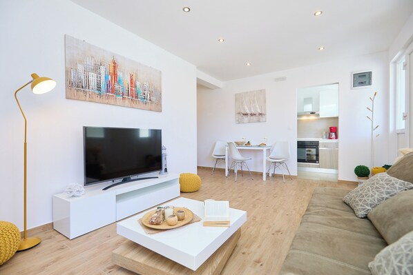 Een moderne woonkamer met een flatscreen televisie, een salontafel met lekkernijen, een bank en een eethoek met een tafel en stoelen.