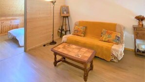 Een knus vertrek met houten wanden en plafond, een bank met kleurrijke kussens, een klein houten tafeltje en een vloerlamp.