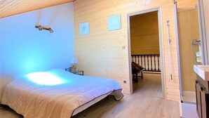 Een slaapkamer met een bed, nachtkastje, houten plafond en een deur naar een andere kamer.