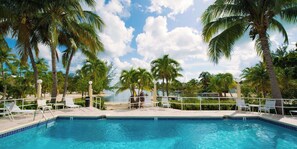 A clear blue pool surrounded by palm trees and lounge chairs, with a view of the beach and ocean in the background. - Rum Point Island House #14, Waterfront, Beach, Pool, Bikes, Kayaks, Paddleboards (Rum Point, North Side)