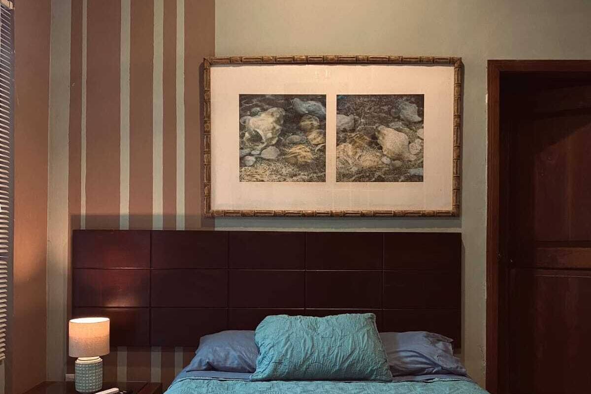 Quarto com cama, mesa de cabeceira, abajur e um quadro na parede.