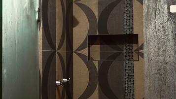 Une salle de bain avec des carreaux aux motifs géométriques, un espace douche et une porte dotée d’une poignée.
