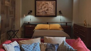 A bedroom with a bed, a red sofa, a ceiling fan, and a framed artwork on the wall. - Casona 13 Flechas (Mazatlán)