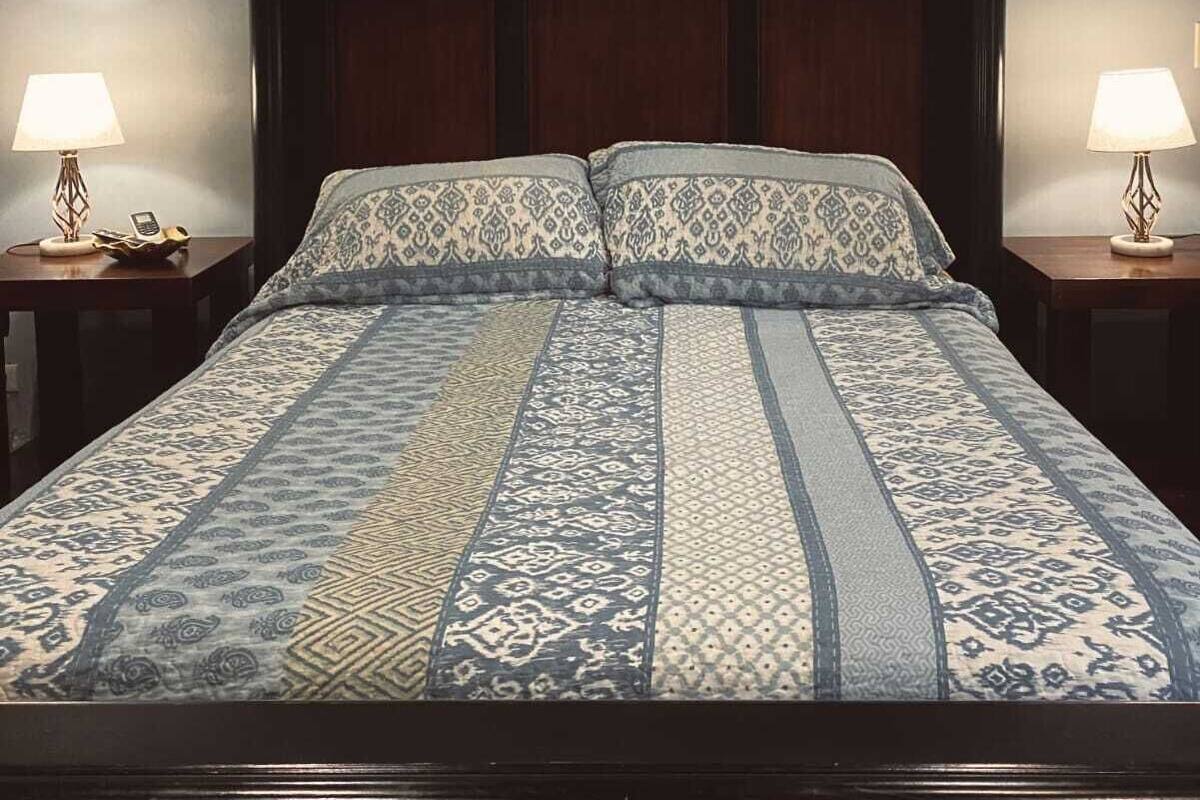 Uma cama com colcha estampada e duas luminárias de cabeceira.