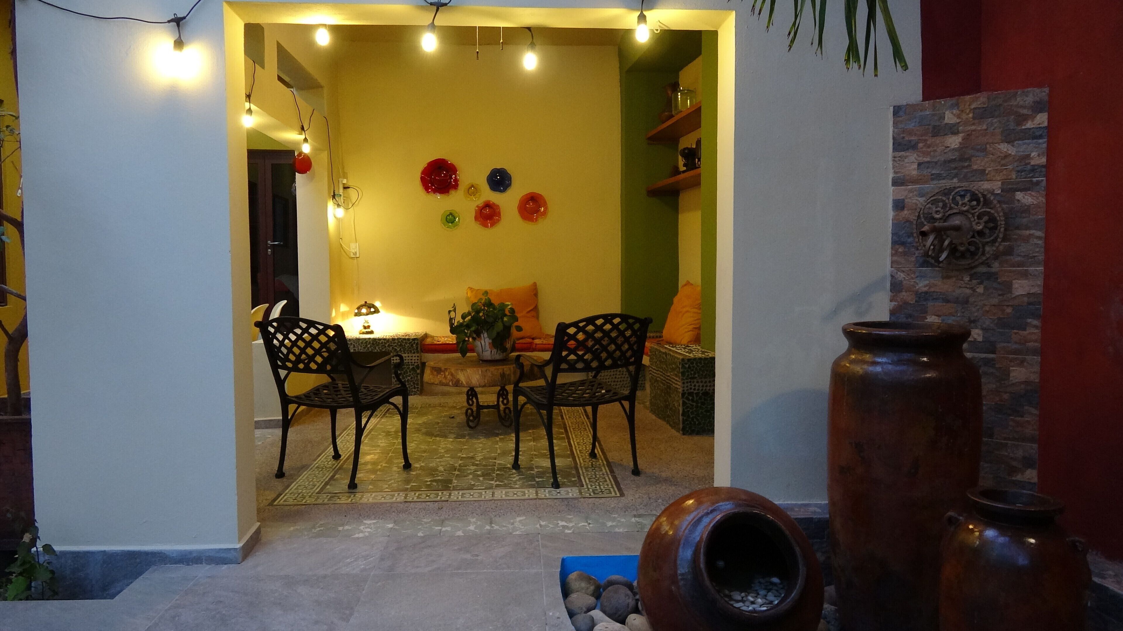 Un espacio interior con comedor que incluye dos sillas, una mesa y una planta en maceta. Se observan elementos decorativos en la pared y un jarrón grande a la derecha.