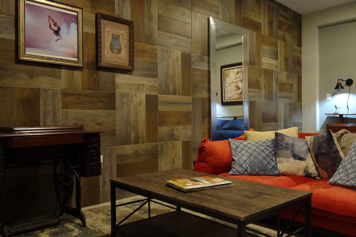 Uma sala de estar com parede de madeira, um sofá com almofadas, uma mesa de centro e uma mesa lateral com abajur.