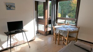 A room with a bed, a dining table with chairs, a TV on a stand, and large windows with curtains. - 2nd floor, balcony, parking, tv, ski locker, 25m², Saint Gervais (Saint-Gervais-les-Bains)