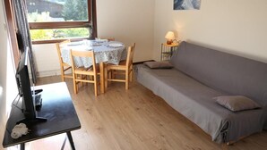 A cozy room with a wooden dining table set for two, a grey sofa, and a TV on a stand. - 2nd floor, balcony, parking, tv, ski locker, 25m², Saint Gervais (Saint-Gervais-les-Bains)
