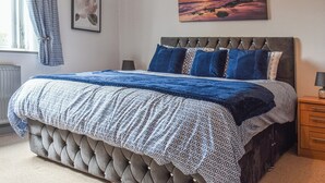 A bedroom with a tufted headboard, patterned bedding, a framed picture, and a sunset painting.