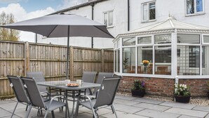 A patio with a table and chairs, a large umbrella, and a conservatory.