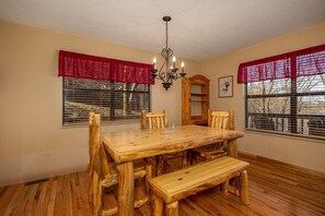 Enjoy meals in this dining room with a wooden table and benches, surrounded by chairs and a chandelier.