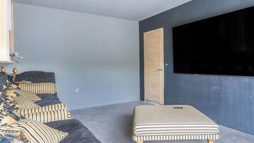 Een moderne woonkamer met een donkere bank, gestreepte kussens, een ottoman met zebraprint, een houten deur en een grote televisie aan de muur.