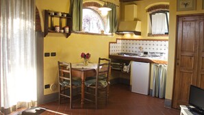 A kitchen with a wooden table, chairs, a refrigerator, a sink, and a window with curtains. - Romantic independent country house with garden, between Lucca and Florence (Toscana)