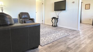 A living room with a dark leather sofa, a patterned rug, and a flat-screen TV mounted on the wall.