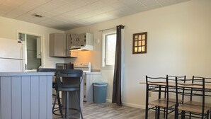 A compact kitchen with a dining area, featuring a bar stool, a table with chairs, and a trash bin.