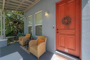 A porch with two wicker chairs, a red door with a wreath, and a small table.