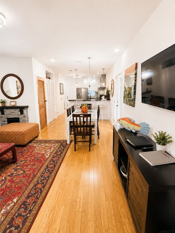 A modern kitchen with white cabinets, a dining table with chairs, a large TV, and a rug.
