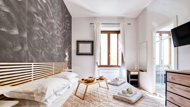 A hotel room with a bed, a bedside table with a tray of breakfast items, a window with curtains, and a TV mounted on the wall. - [3 bathroom] Lovely Apartment in the Vatican, close to Castel Sant'Angelo (Roma)