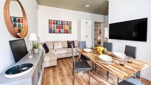 A modern living room with a sofa, a dining table set for four, a TV mounted on the wall, and a large mirror. - [3 bathroom] Lovely Apartment in the Vatican, close to Castel Sant'Angelo (Roma)