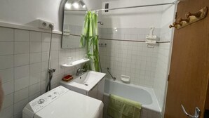 Un baño compacto con lavamanos blanco, un espejo, ducha e inodoro.