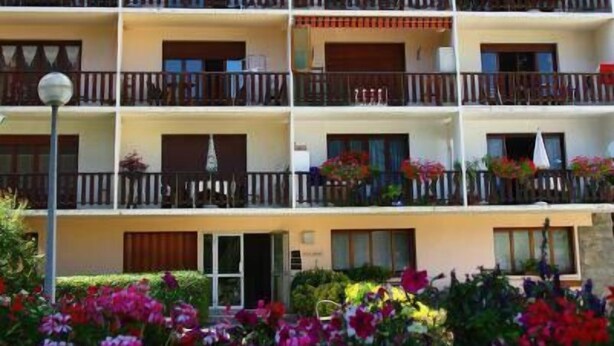 Un hotel de varios pisos con balcones, mobiliario exterior y una variedad de flores en primer plano.
