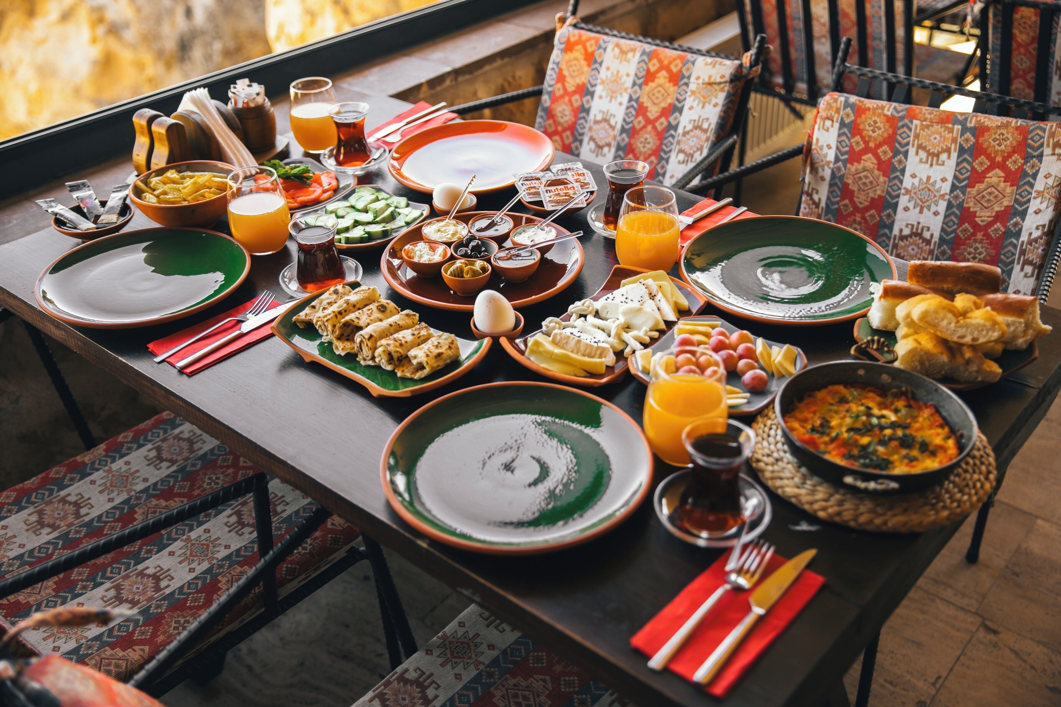 Une table à manger dressée avec différents plats, notamment du pain, du fromage et un bol de soupe, et offrant une vue sur l’extérieur.