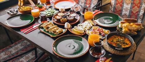 Une table à manger dressée avec différents plats, notamment du pain, du fromage et un bol de soupe, et offrant une vue sur l’extérieur.