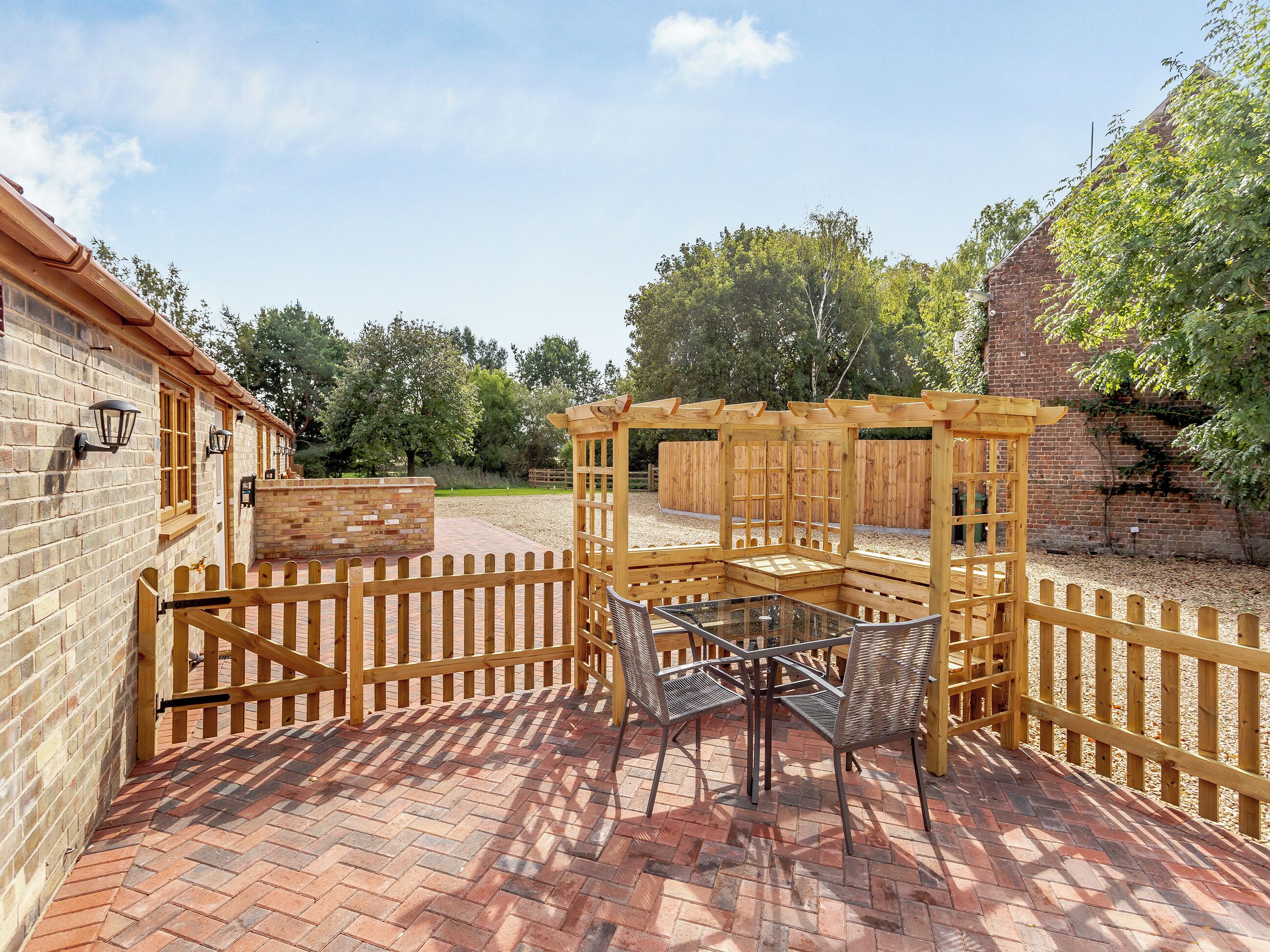 Un patio con una pérgola de madera, una mesa con sillas y un muro de ladrillo.