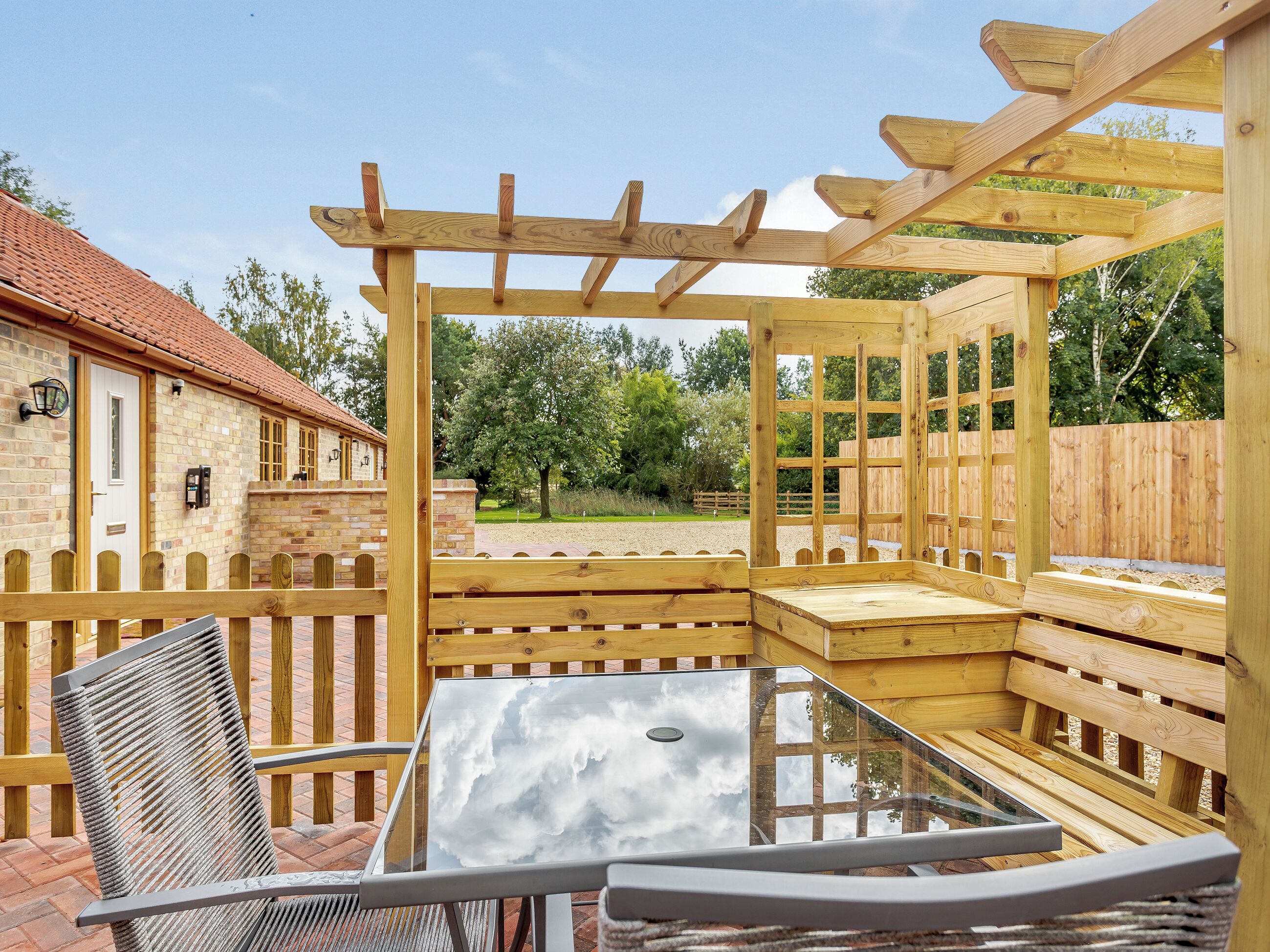 A wooden pergola structure with a glass table and metal chairs.
