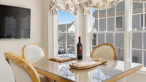 Un coin repas avec une table en verre, des chaises en bois, une bouteille de vin et un lustre.