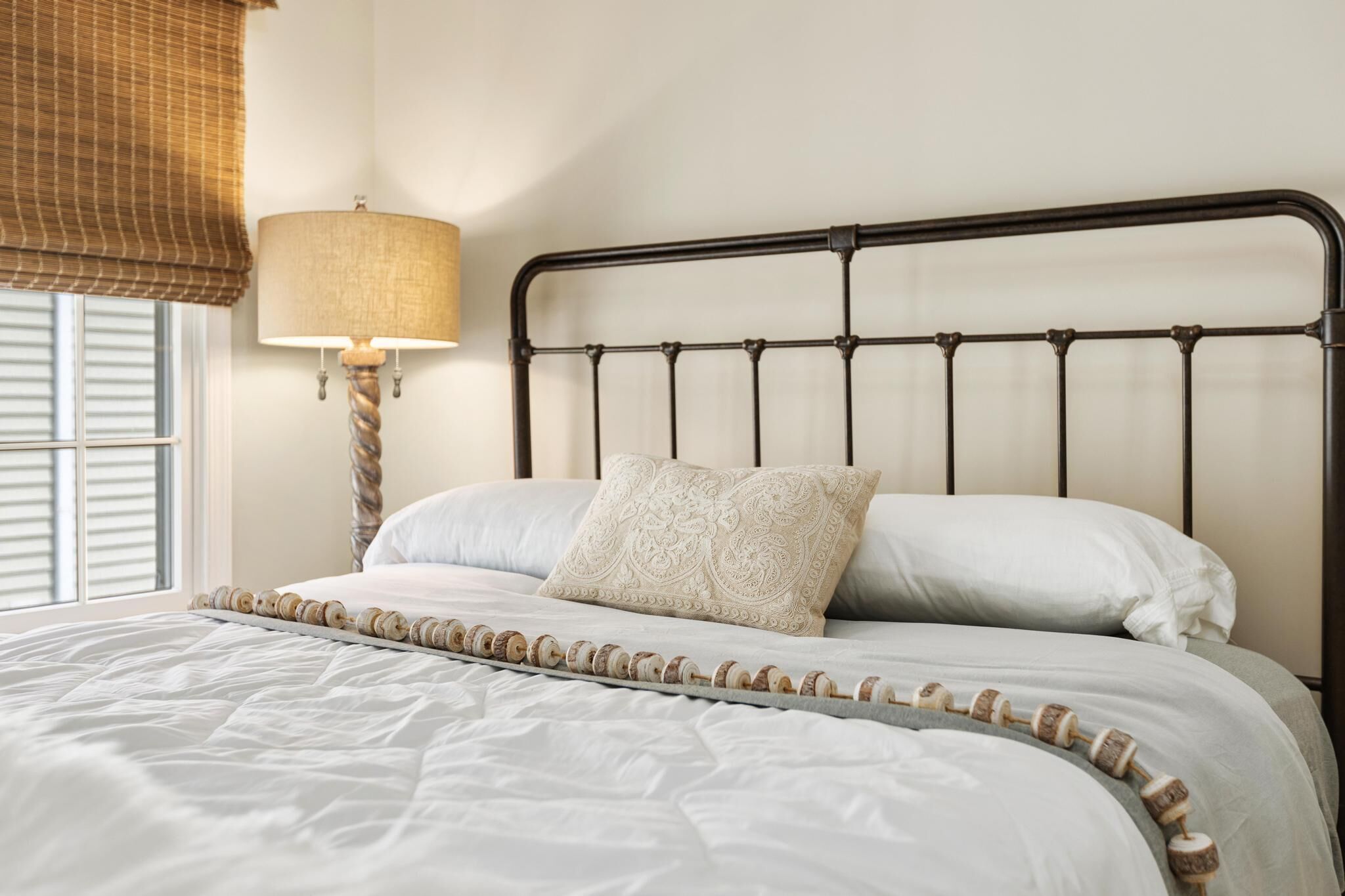 Un lit bien fait, avec une tête de lit en métal, un coussin décoratif à motifs et une lampe de chevet.