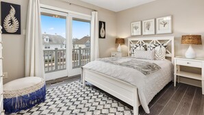 Une chambre à coucher comprenant un lit, une table de chevet, une lampe, une fen être avec des rideaux et une vue sur les maisons à l’extérieur.