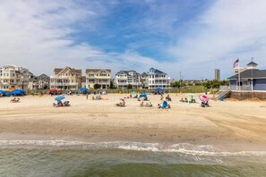 A beach with multiple beach umbrellas and people relaxing. There are several multi-story buildings in the background.