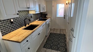 Cocina compacta con armarios blancos, un salpicadero blanco y negro, encimera de madera y alfombra estampada.