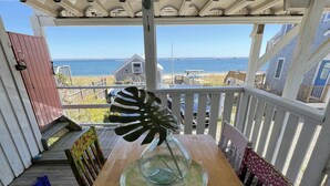 Terraza de madera con mesa y sillas, con vista a una playa y el océano.