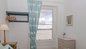 A bedroom with a bed, a nightstand, a dresser, a window with a view of a body of water, and a curtain with a pattern. - Crow's Nest (Carnforth)