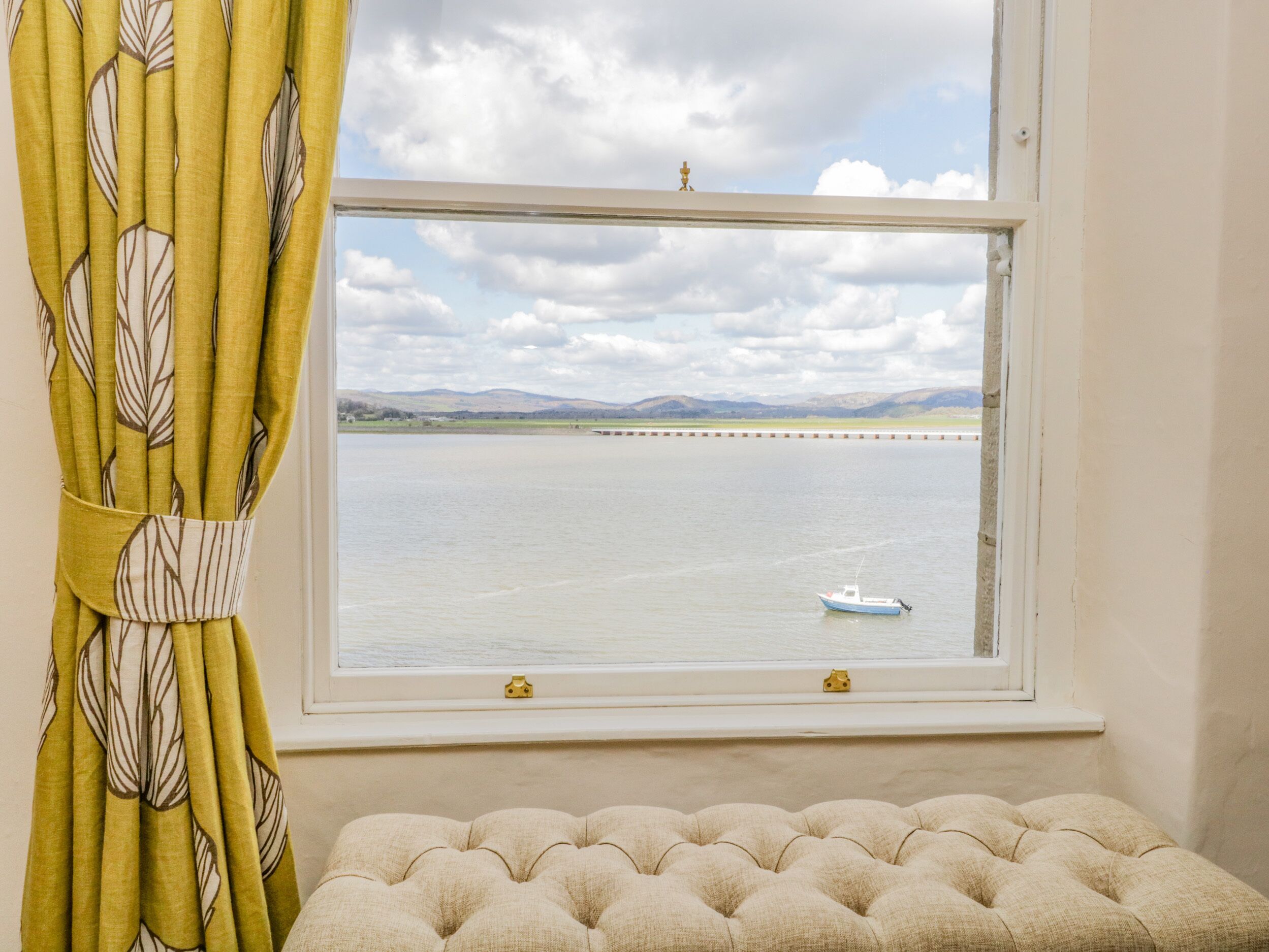 A window with a view of a calm body of water, a small boat, and distant hills.