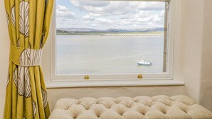 A window with a view of a calm body of water, a small boat, and distant hills. - Crow's Nest (Carnforth)