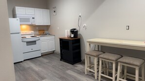 A compact kitchen with white cabinets, a microwave, and a stove. There's a small black cabinet with a coffee maker and a wooden table with three stools. - Cozy studio just 5 min. Away from Coachella fest (Coachella)