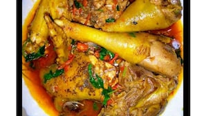 Un plato con muslos de pollo y verduras en salsa.